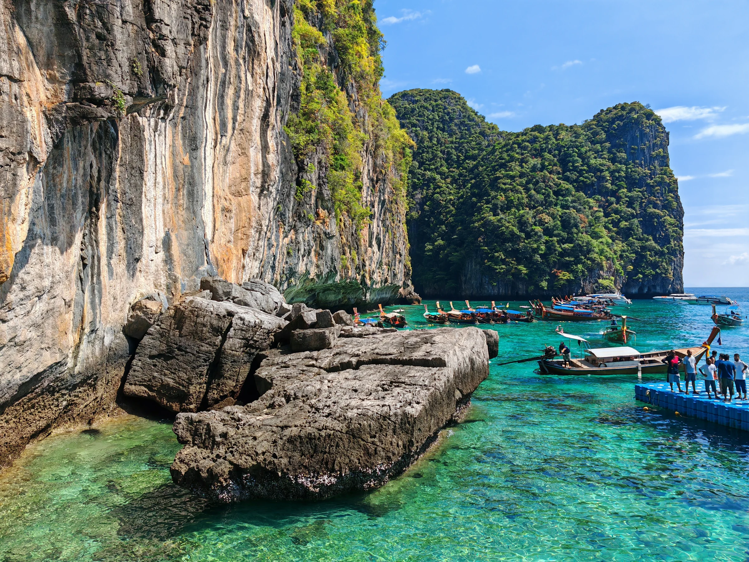 Longtail boats beside towering limestone cliffs and clear turquoise water