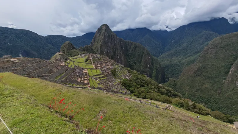 Machu Picchu terraces and stone ruins beneath a steep mountain and cloud-covered peaks
