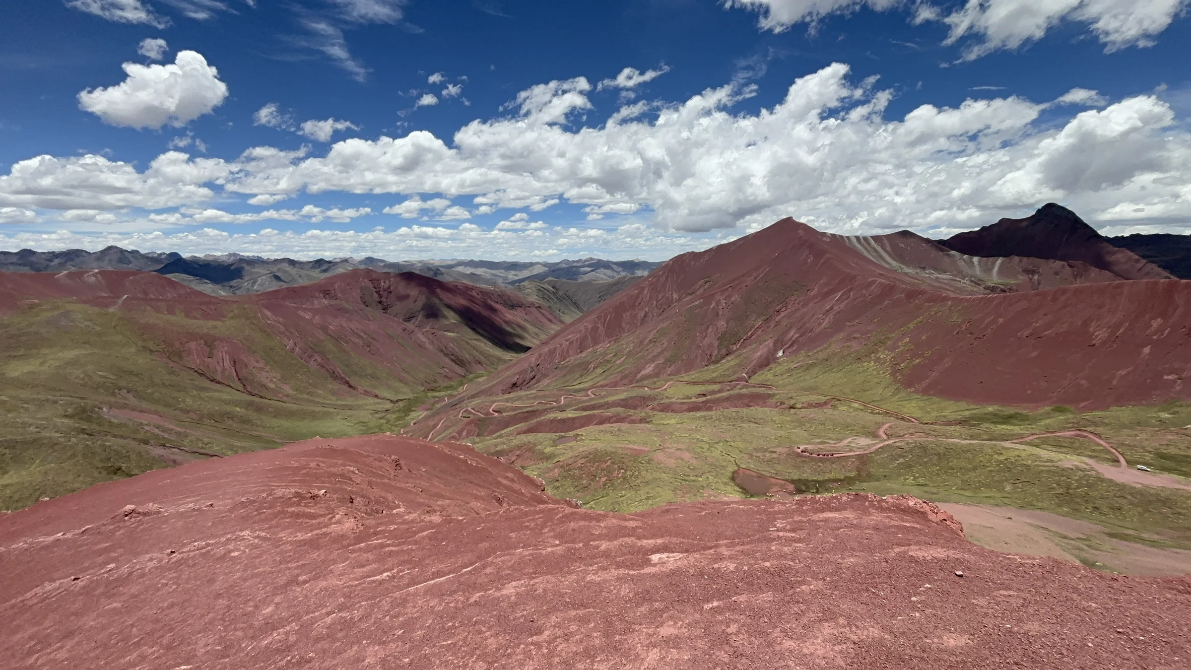 Red and green mountain ridges under scattered clouds near Rainbow Mountain