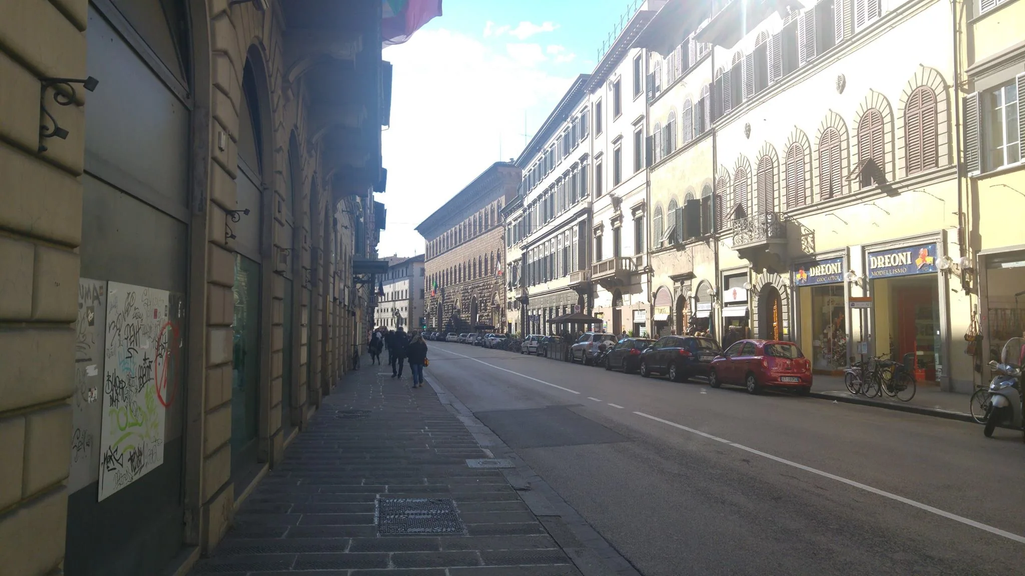A sunlit Florence street lined with pale buildings