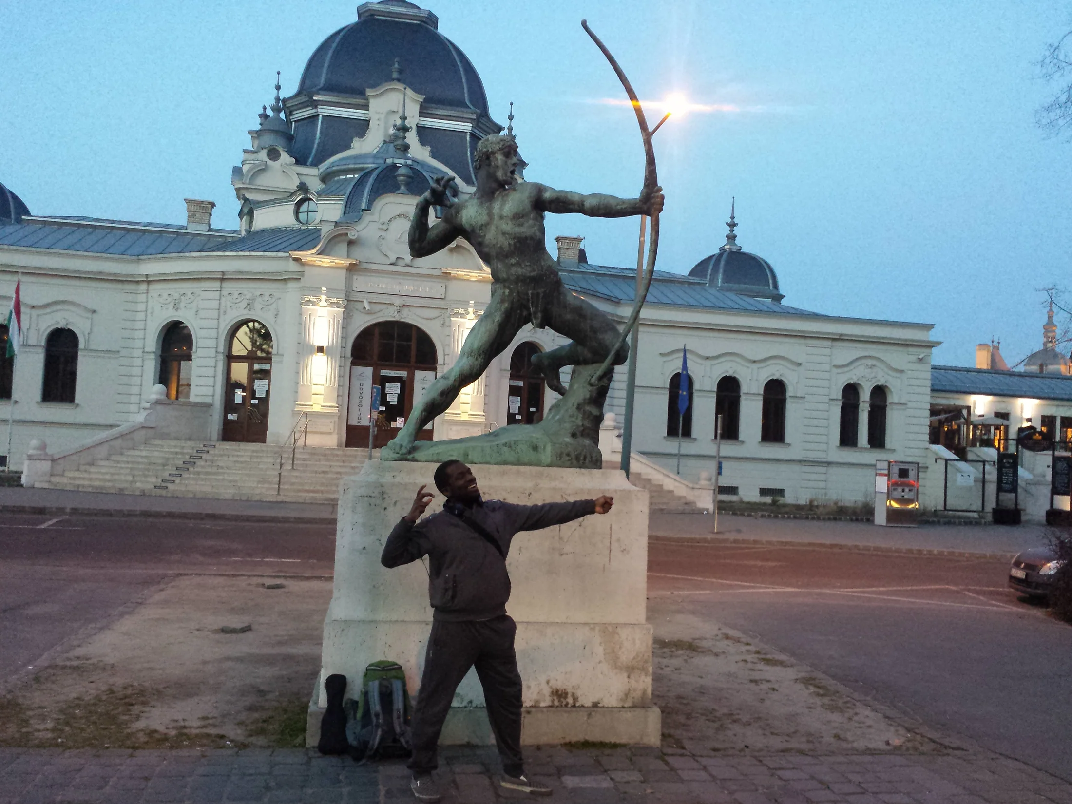 A traveller posing near an archer statue and a pale building