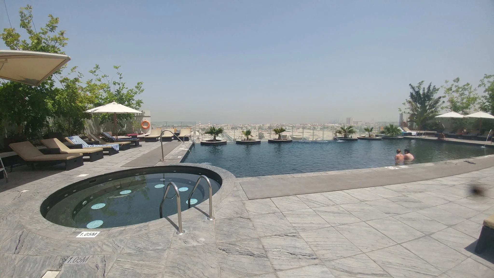 An outdoor pool and shaded loungers beneath a hazy sky