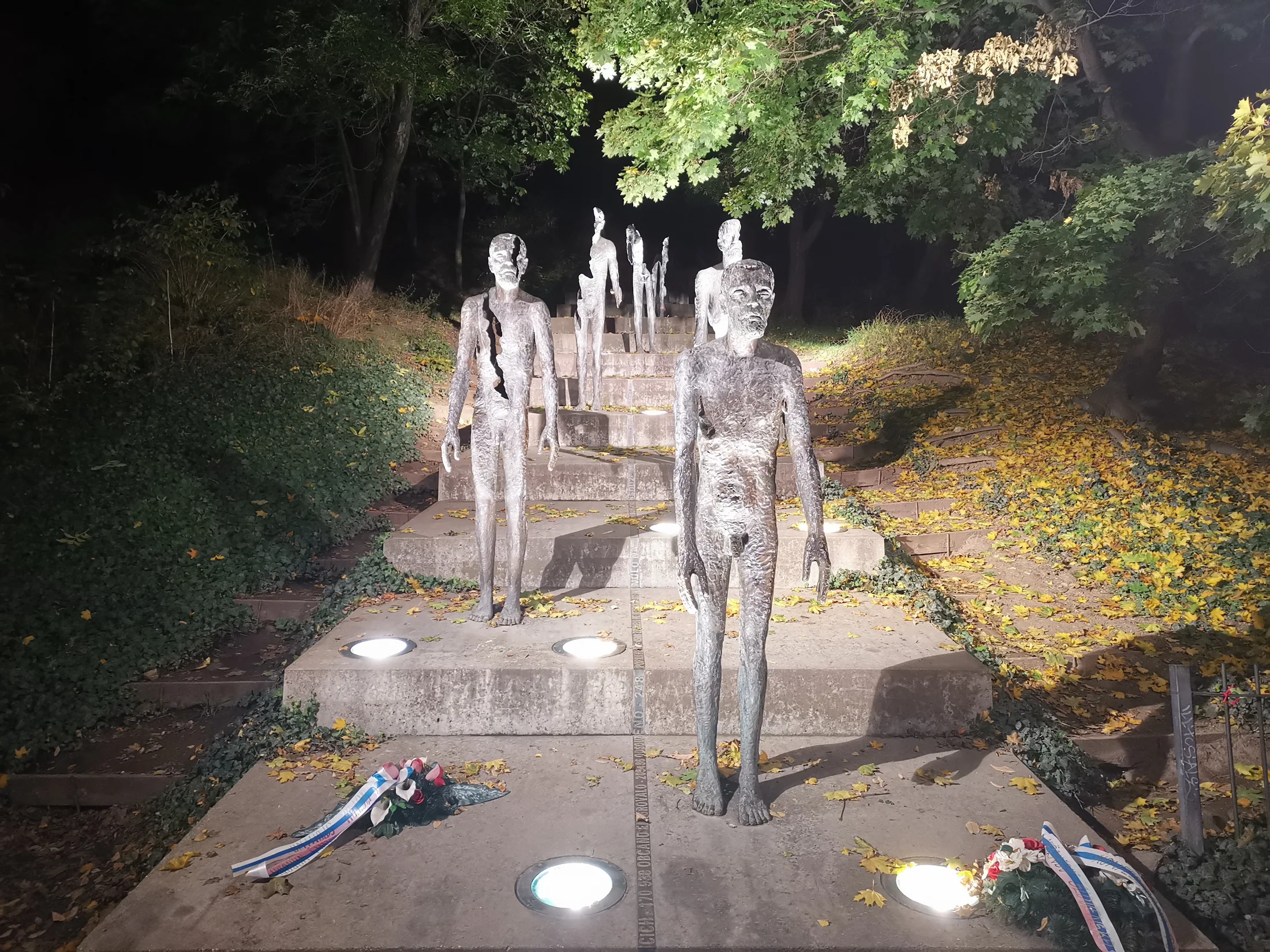 A line of memorial sculptures on steps beneath trees
