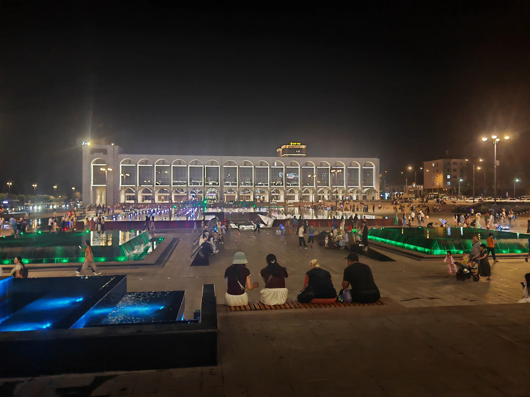 People gathering in an illuminated Bishkek square at night